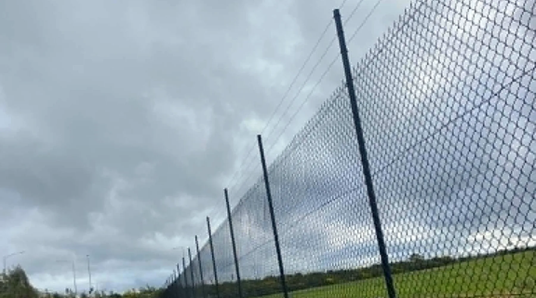 High black chain-mesh perimeter fencing installed across a sloping site