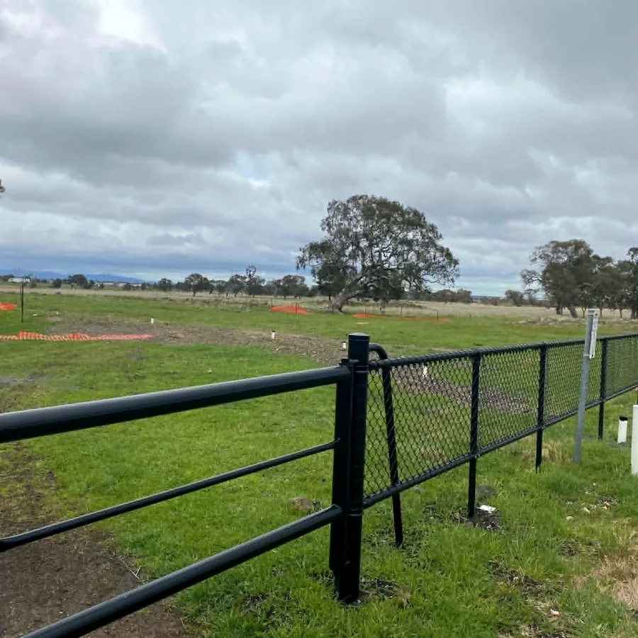 Black tubular rail and chain-mesh fencing meeting along a boundary