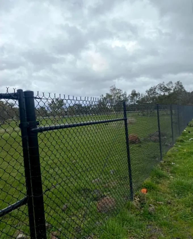 Close view of a black chain-mesh gate post and top rail