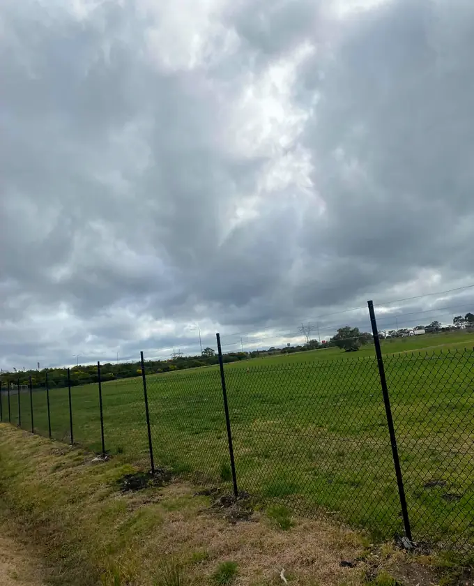 Long run of black chain-mesh perimeter fencing across open grassland