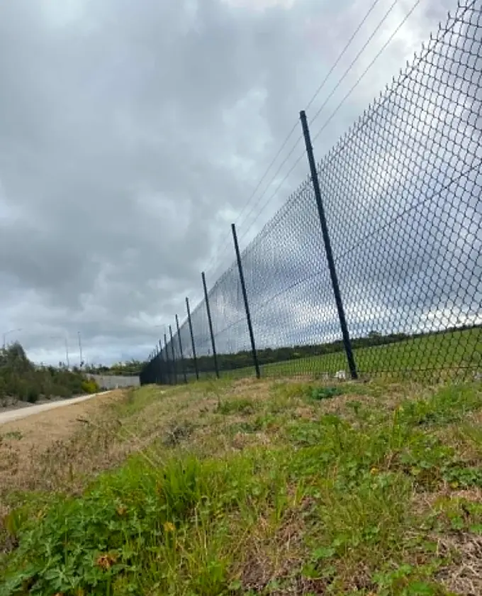 Black chain-mesh security fence extending along a sloping site