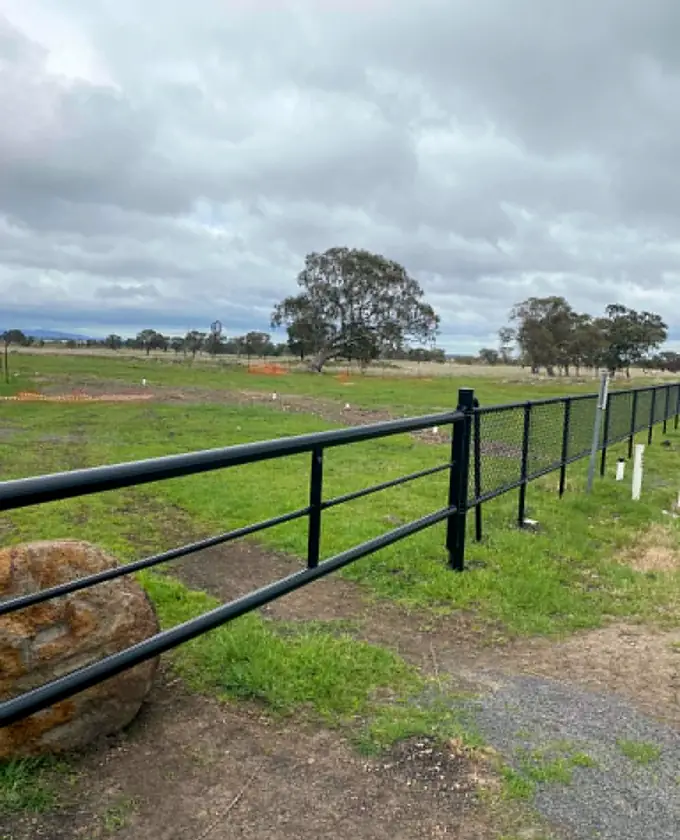 Black tubular rail fence running beside an open site