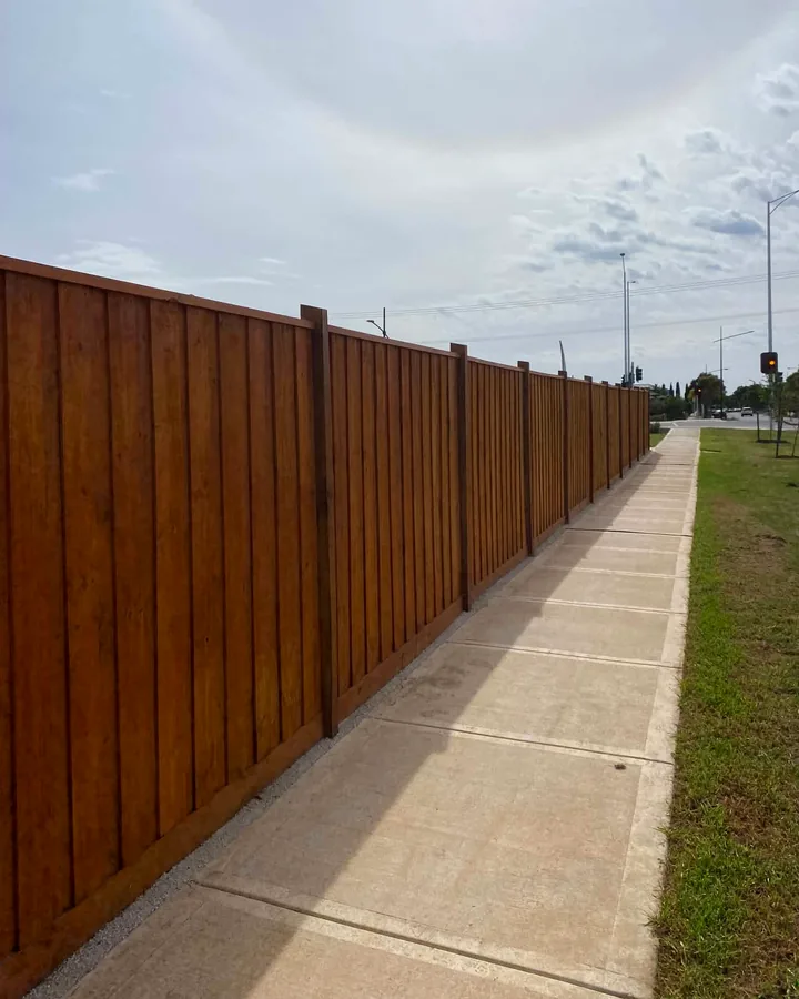 Long stained timber boundary fence installed beside a concrete footpath