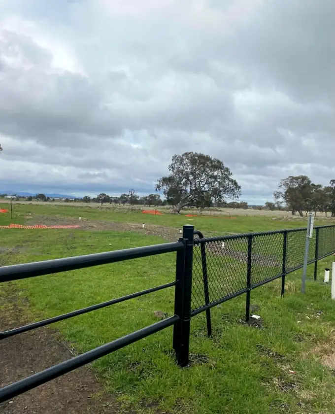 Black tubular rail and chain-mesh fencing meeting along a boundary
