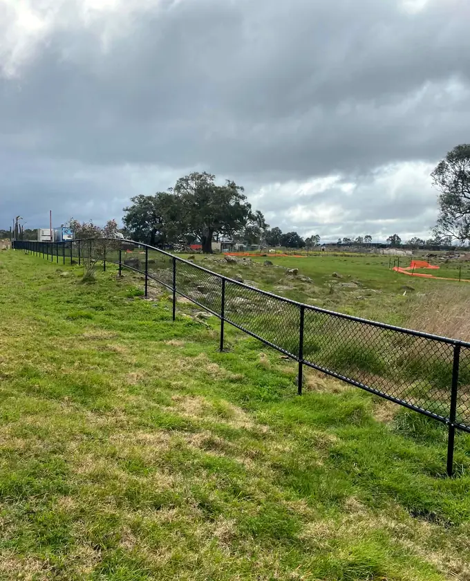 Black chain-mesh fencing installed across a sloping open site