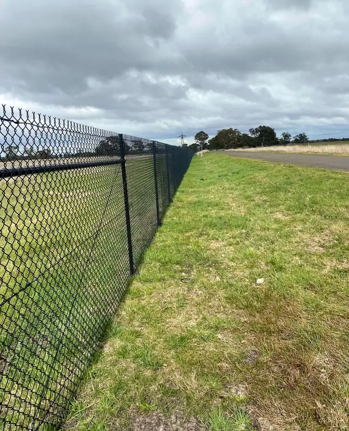Black chain-mesh boundary fence extending beside an access road